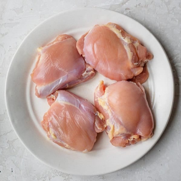 Four chicken thighs on a plate.