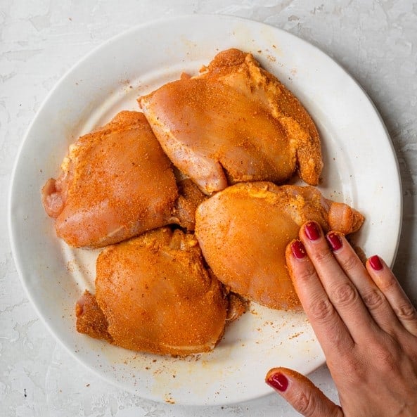 A hand rubbing the seasoning into the chicken thighs.