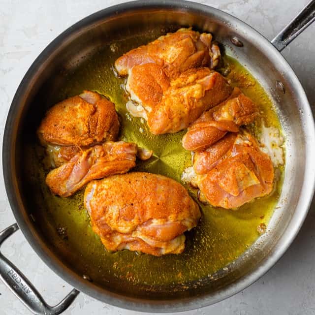 Four chicken thighs in an oiled skillet before cooking.