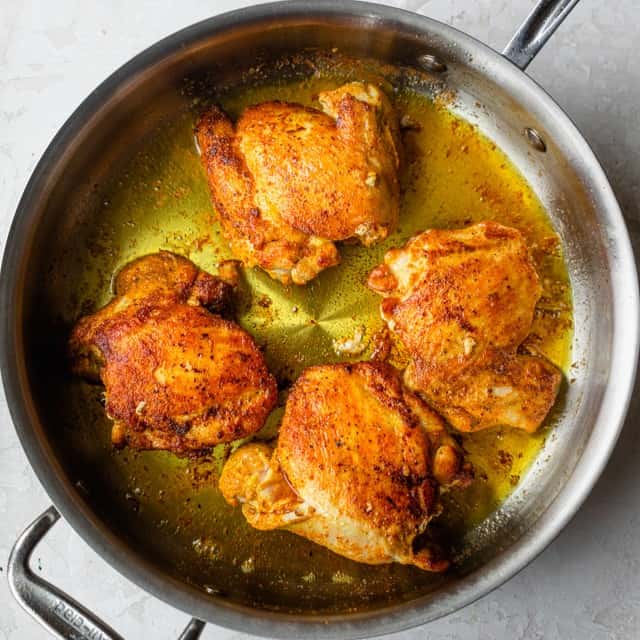 Four chicken thighs in a skillet after cooking.