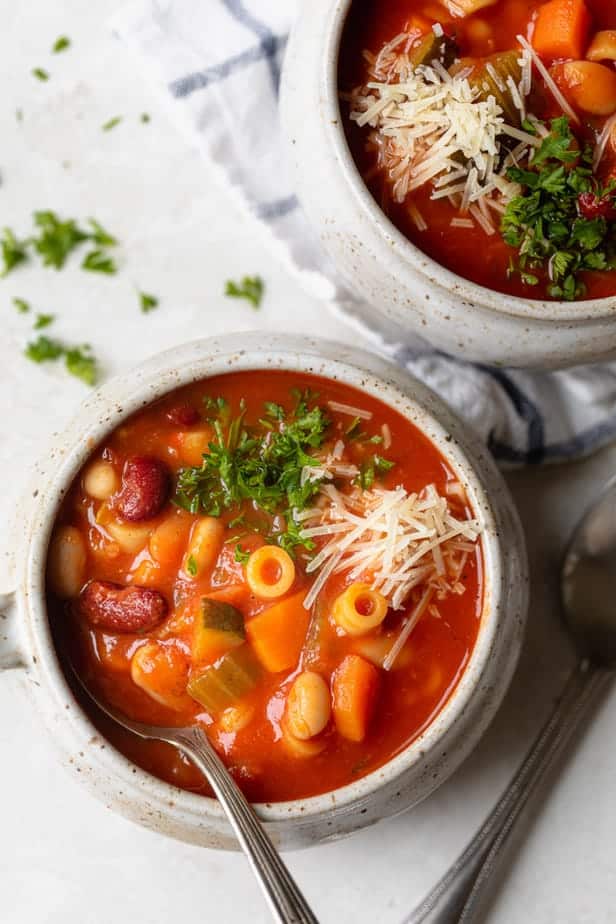 Close up of mug bowl of vegetarian minestrone soup topped with parsley and parmesan cheese