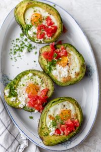 Bakes eggs in avocado garnished with tomatoes, feta cheese and parsley