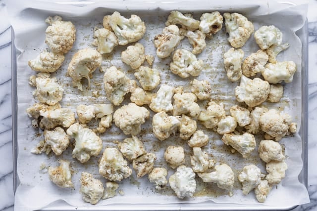 Cauliflower florets on a baking tray with spices and olive oil before roasting