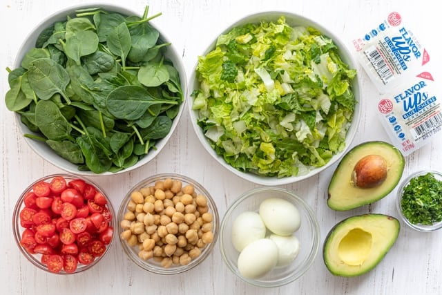 Ingredients to make the vegetarian cobb salad: spinach, lettuce, tomatoes, chickpeas, eggs, avocado, parsley and blue cheese