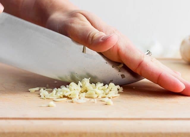Hand mincing garlic with large chef's knife