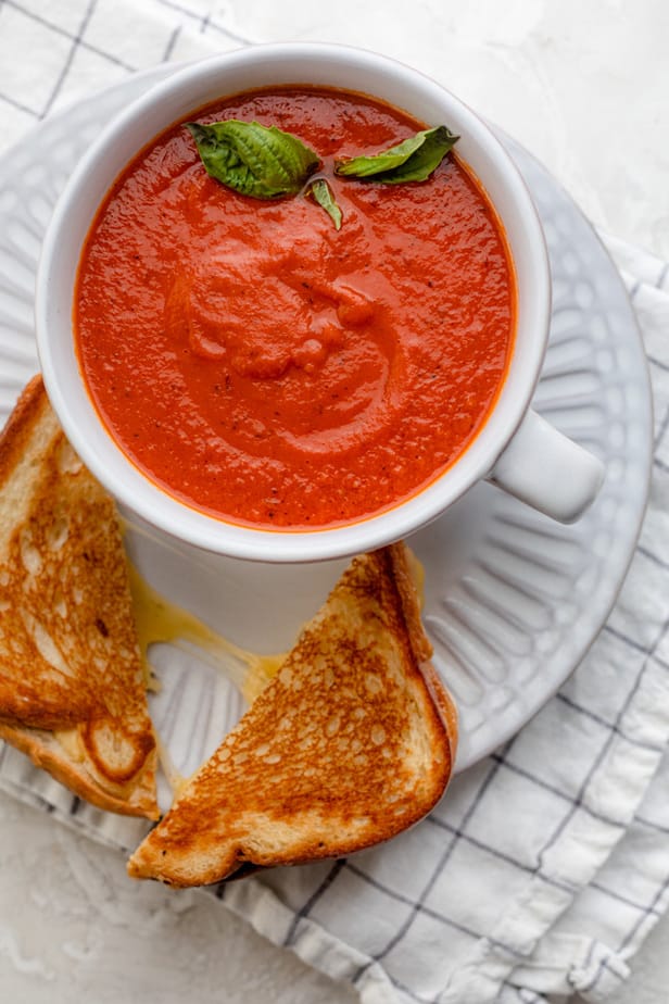 Grilled cheese on a white plate with bowl of tomato soup