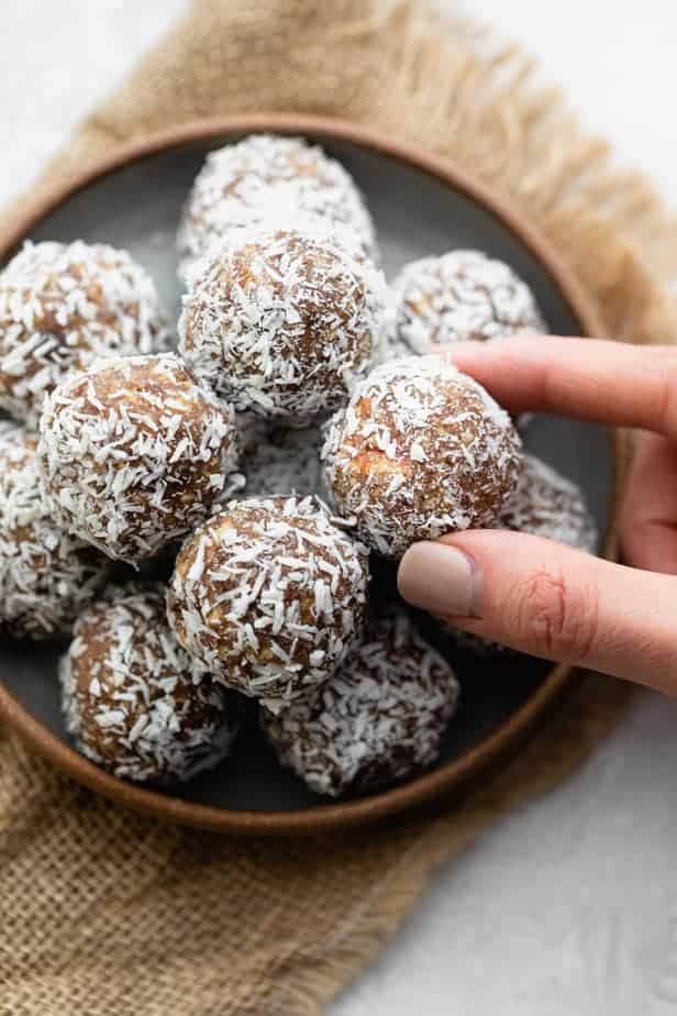 Hand grabbing one of the coconut date balls from shallow bowl