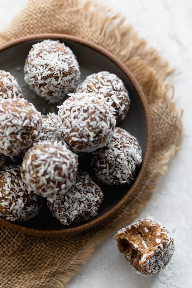 Bowl of coconut date balls with one on the table with bite taken