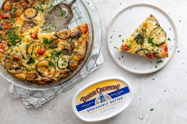 A slice of crustless quiche on a plate next to a baking dish containing the rest of the quiche