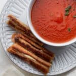 Grilled cheese dippers on a plate next to bowl of tomato soup