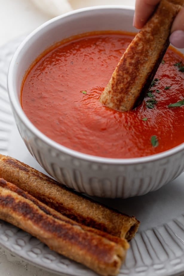 Grilled cheese dippers going into bowl of tomato soup