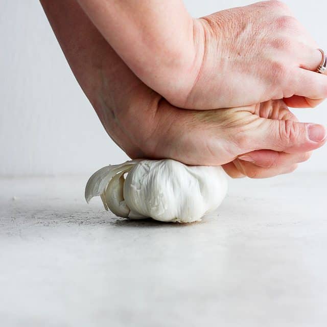 two hands pressing down on a bulb of garlic