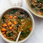 Two bowls of lentil kale soup with a spoon inside one bowl