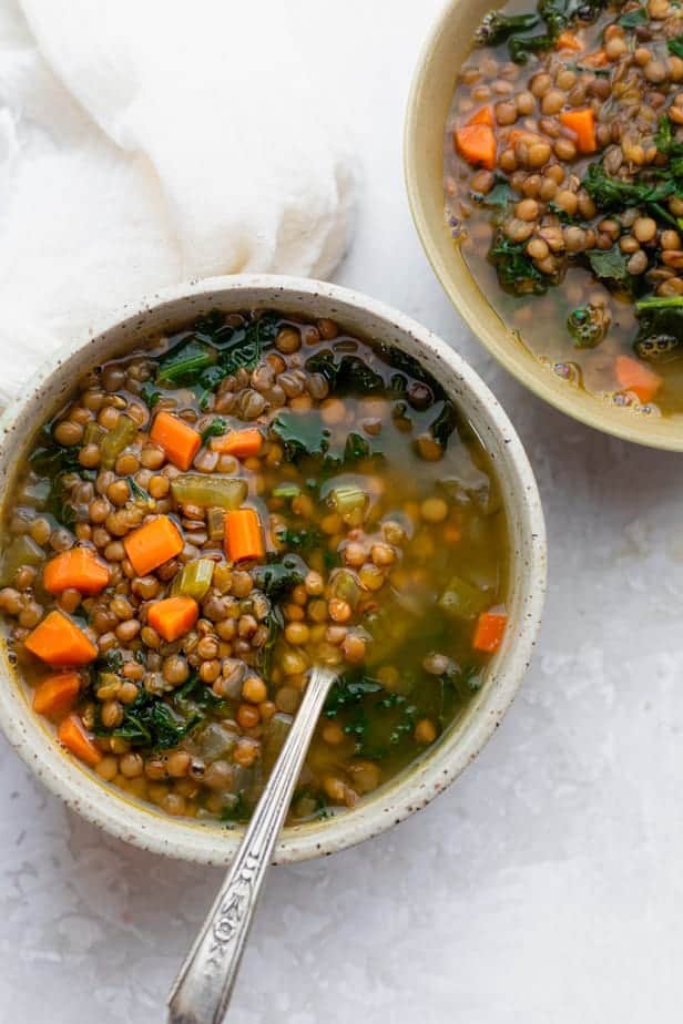 Two bowls of lentil kale soup with a spoon inside one bowl