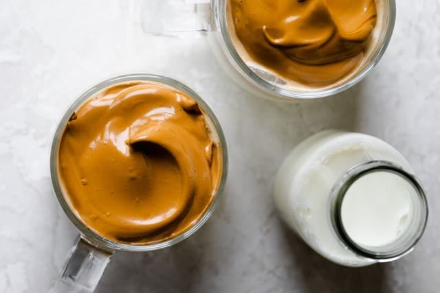 Adding the whipped coffee on top of iced milk in a glass mug