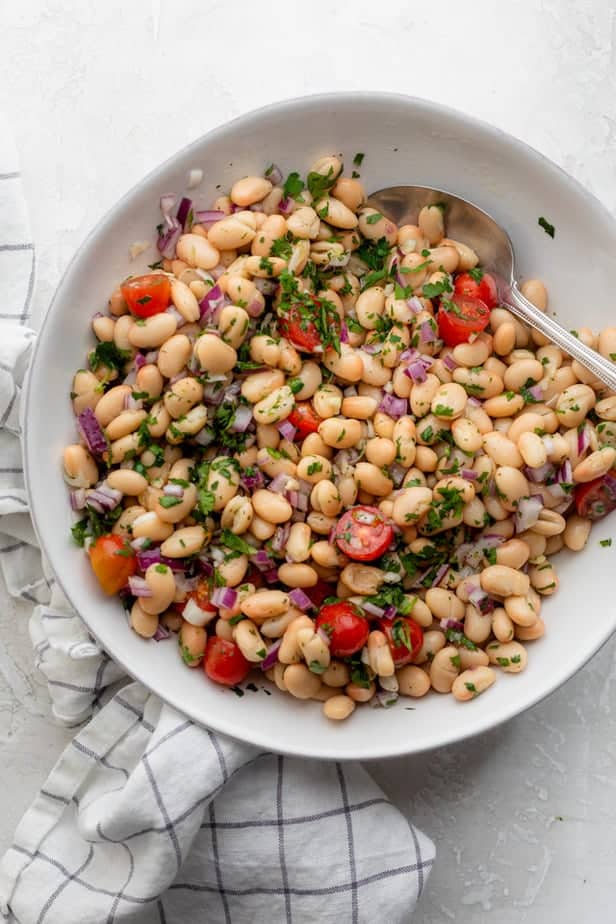 White bean salad in a white bowl with a spoon