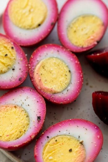 A plate of beet pickled eggs cut in half, with beets nearby.