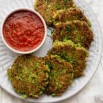 Broccoli fritters on a white plate with a dipping sauce