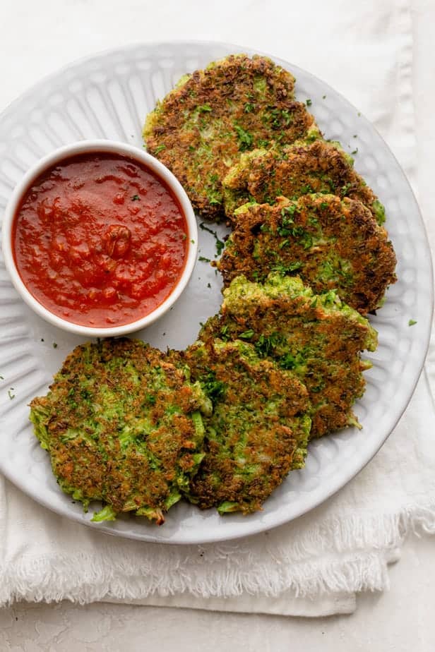 Broccoli fritters on a white plate with a dipping sauce