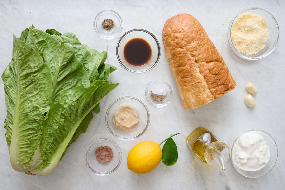 Ingredients for recipe before prepping: French baguette, oil, spices, garlic cloves, anchovy paste, grated parmesan, Dijon mustard, Worcestershire sauce.