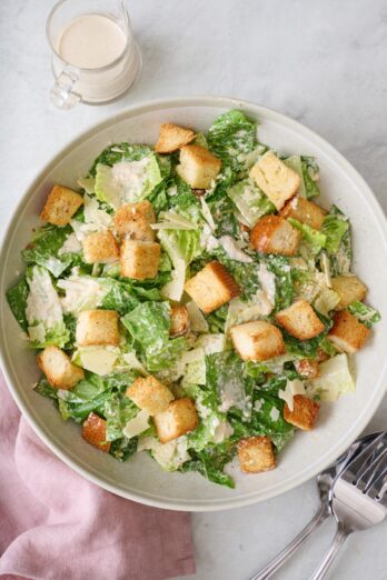 Classic Caesar salad in a large salad bowl with an extra jar of dressing nearby.