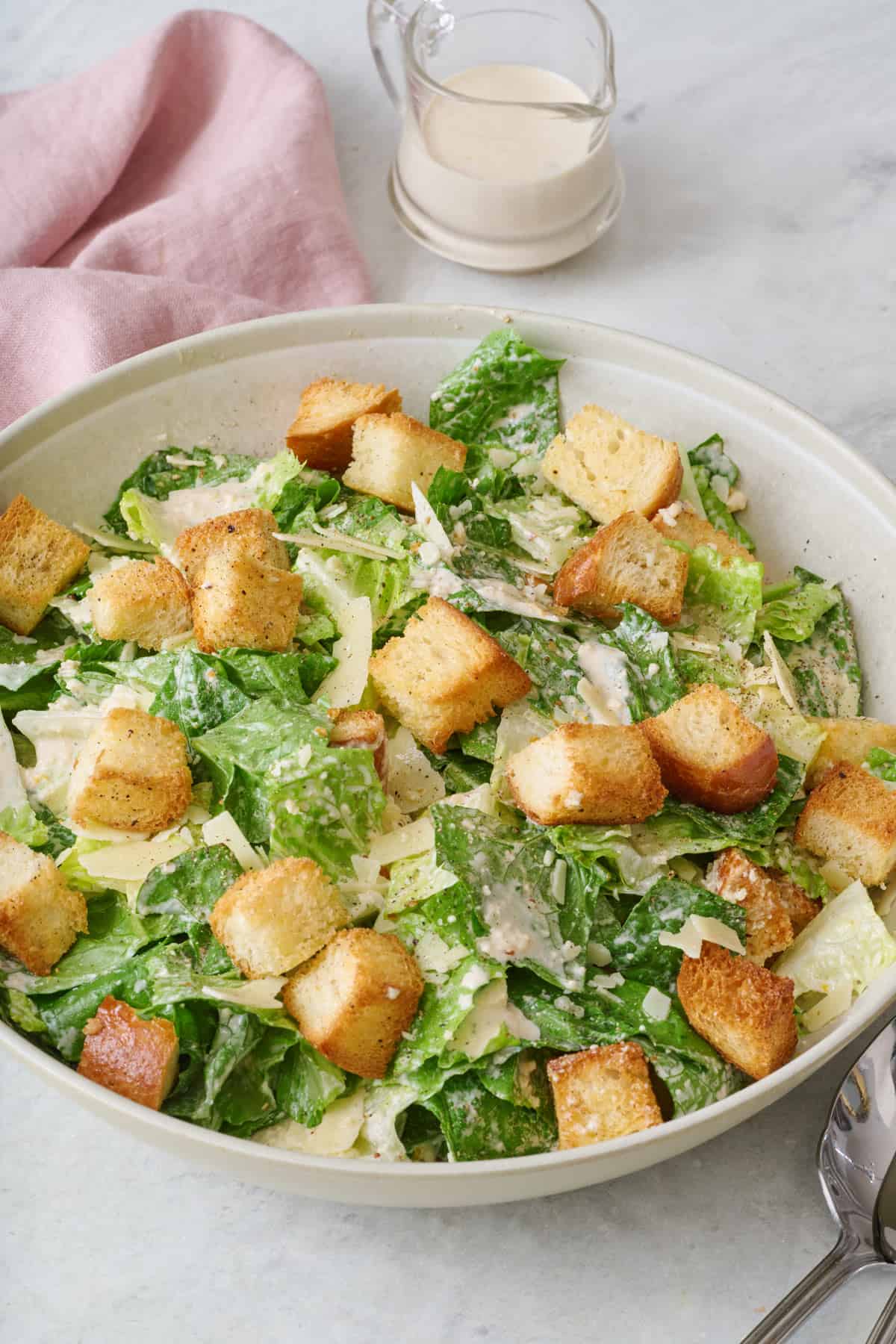 Homemade Caesar salad in a large salad bowl with an extra jar of dressing nearby.