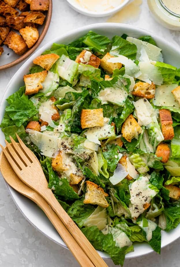 Caesar salad in a white bowl with wooden salad servers