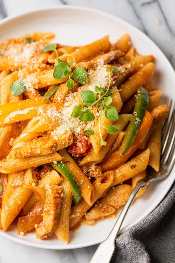 Chicken fajita pasta on a white plate with a fork on the plate