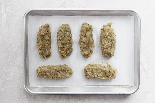 Chicken patties with herbs and spices on baking sheet before cooking