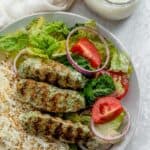 Chicken kafta on a plate with rice and salad along with garlic sauce on the side
