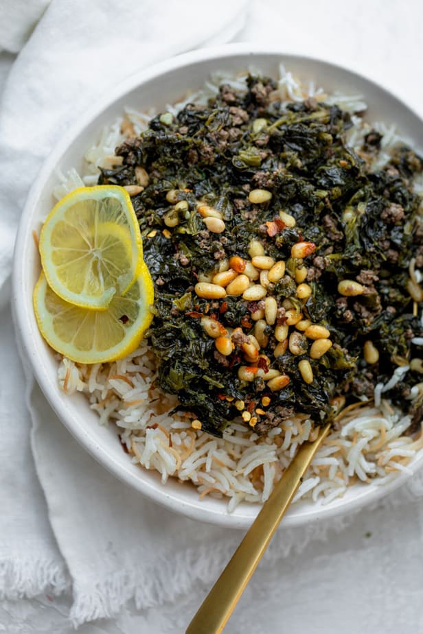 Lebanese spinach stew (sabanekh) served over rice with lemon slices and pine nuts