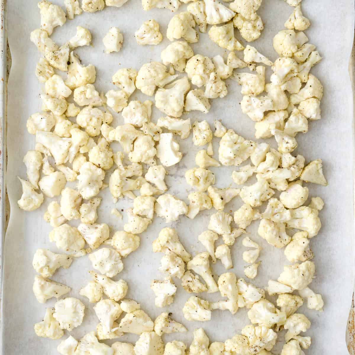 Cauliflower tossed in oil, salt and pepper on a parchment lined baking sheet.