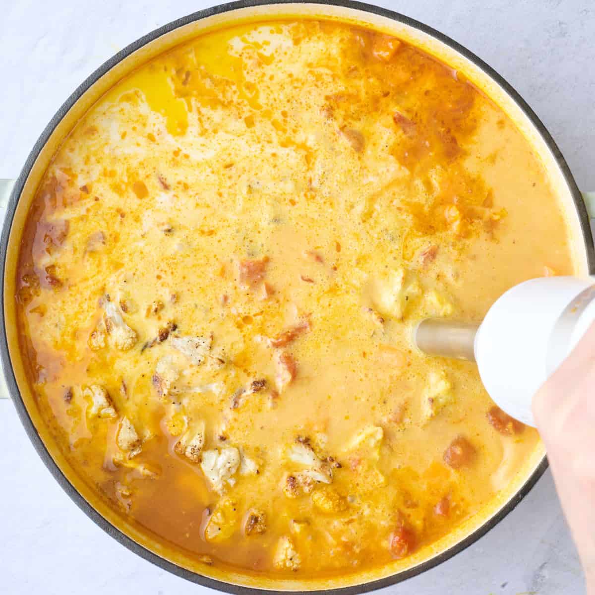 Immersion blender dipped inside with partially blended soup.
