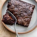 Zucchini brownie square on a plate with fork cutting into one