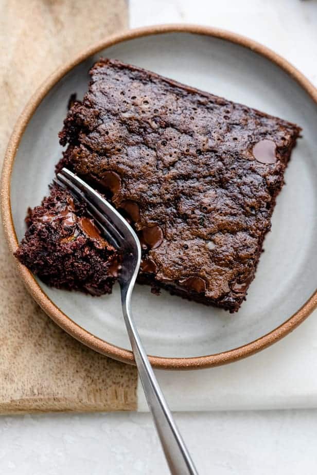 Zucchini brownie square on a plate with fork cutting into one