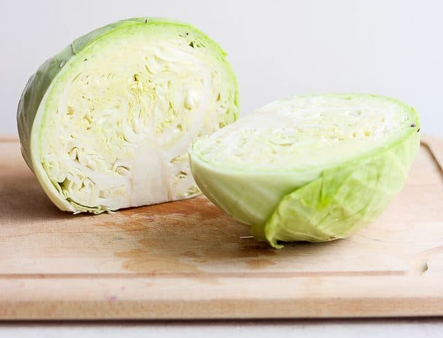 Green cabbage sliced in half on cutting board