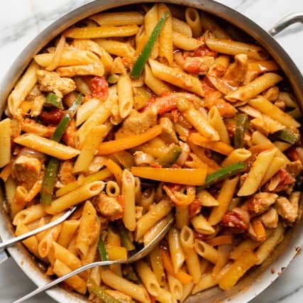 Chicken fajita pasta in a large pan with tongs resting on top.
