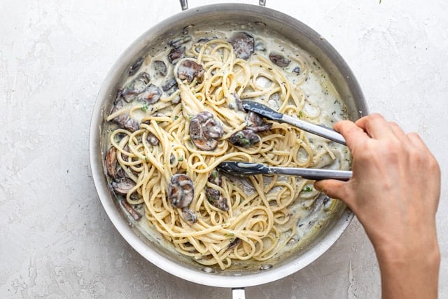 hand with tongs mixing a pot of creamy mushroom pasta