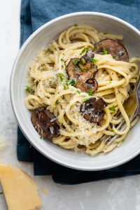 Creamy garlic mushroom pasta in a bowl with parmesan cheese next to it