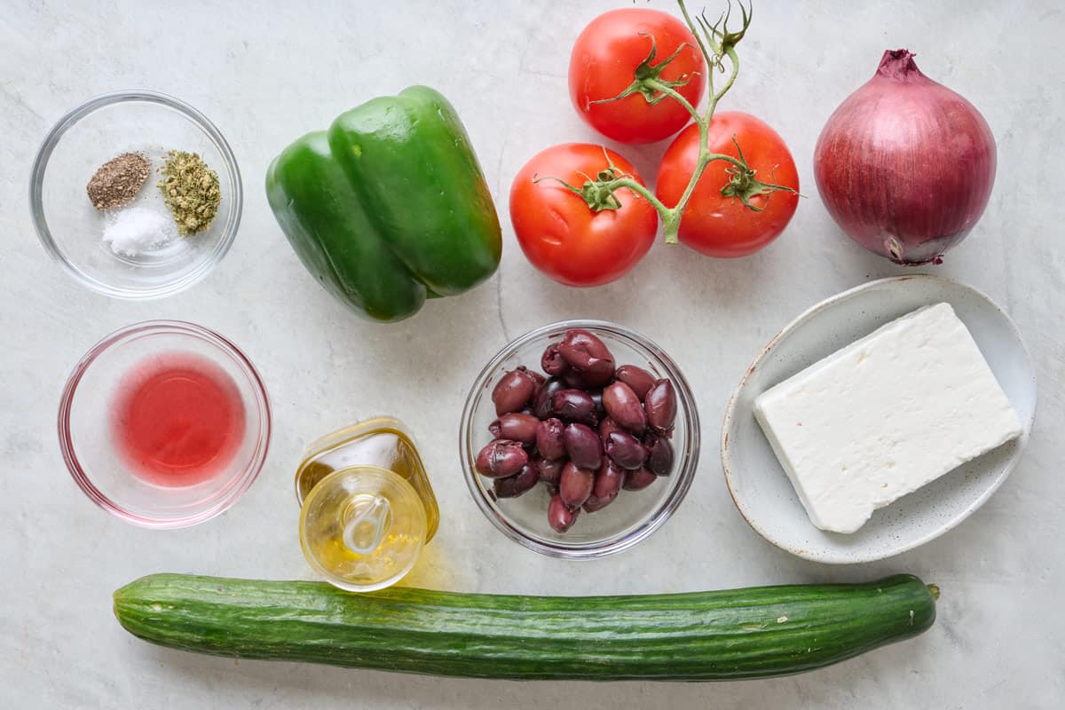 Ingredients for recipe: green pepper, tomatoes, onion, kalamative olives, cucumber, feta, oil, vinegar, and spices.