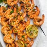 Grilled shrimp skewers on a white plate with grilled lemon slices