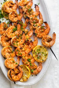 Grilled shrimp skewers on a white plate with grilled lemon slices