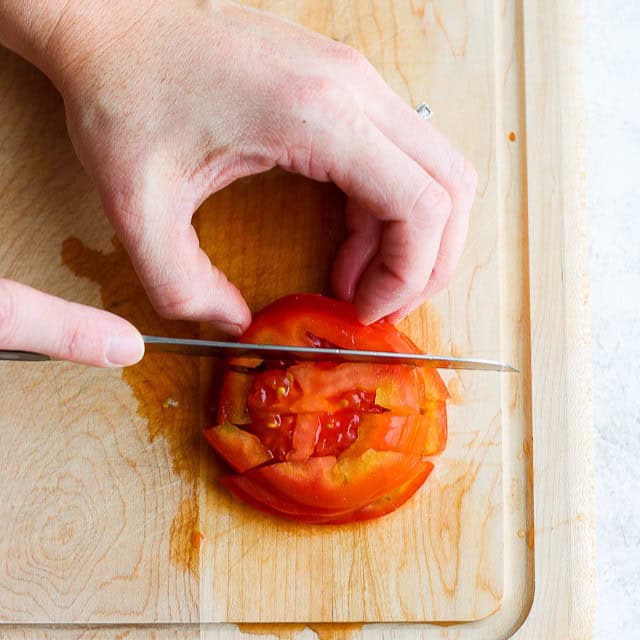 Tomato slices stacked on top of each other with a knife cutting downwards.