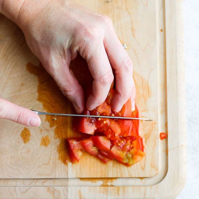 Tomato slices stacked on top of each other with a knife cutting downwards.