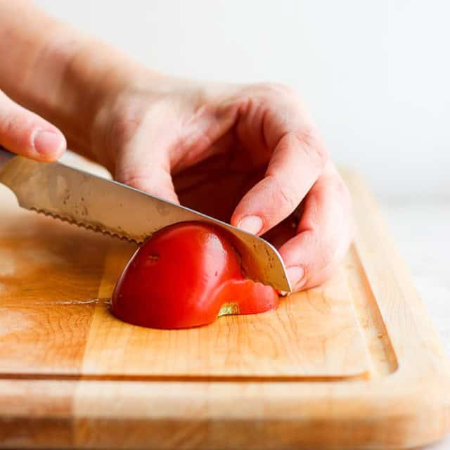 Half of tomato laid on the cutting board being cut in half again.
