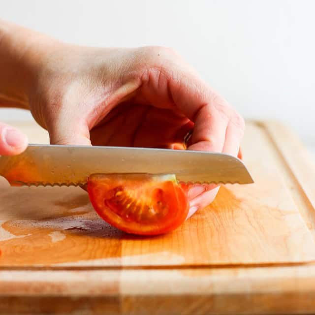 Half of tomato laid on the cutting board being cut in half again.