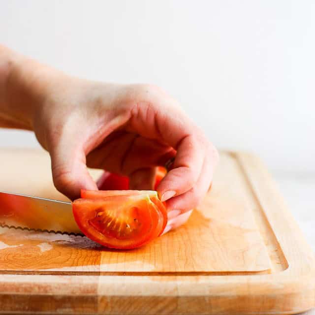 Half of tomato laid on the cutting board being cut in half again.