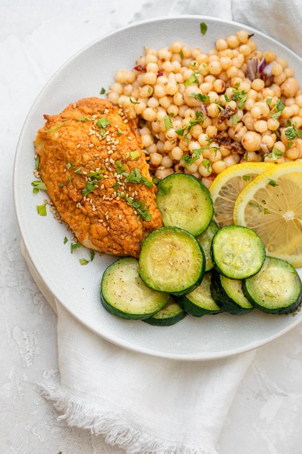 Hummus crusted chicken on a plate with zucchini slices and couscous