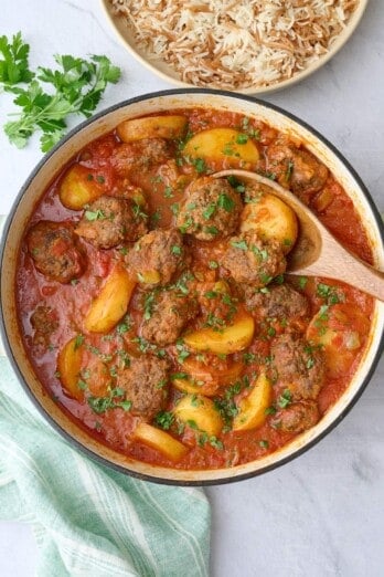 Kafta Potato Stew in the pot garnished lightly with chopped parsley, serving spoon, small dish of chopped parsley, and serving dish of Lebanese rice nearby.