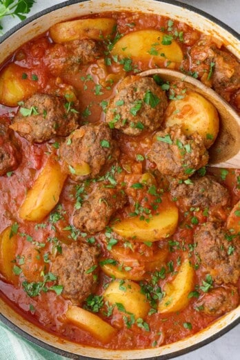 Kafta Potato Stew in the pot garnished lightly with chopped parsley, serving spoon, small dish of chopped parsley, and serving dish of Lebanese rice nearby.